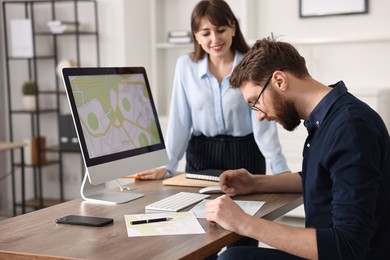 Cartographers working with cadastral map on computer at table in office