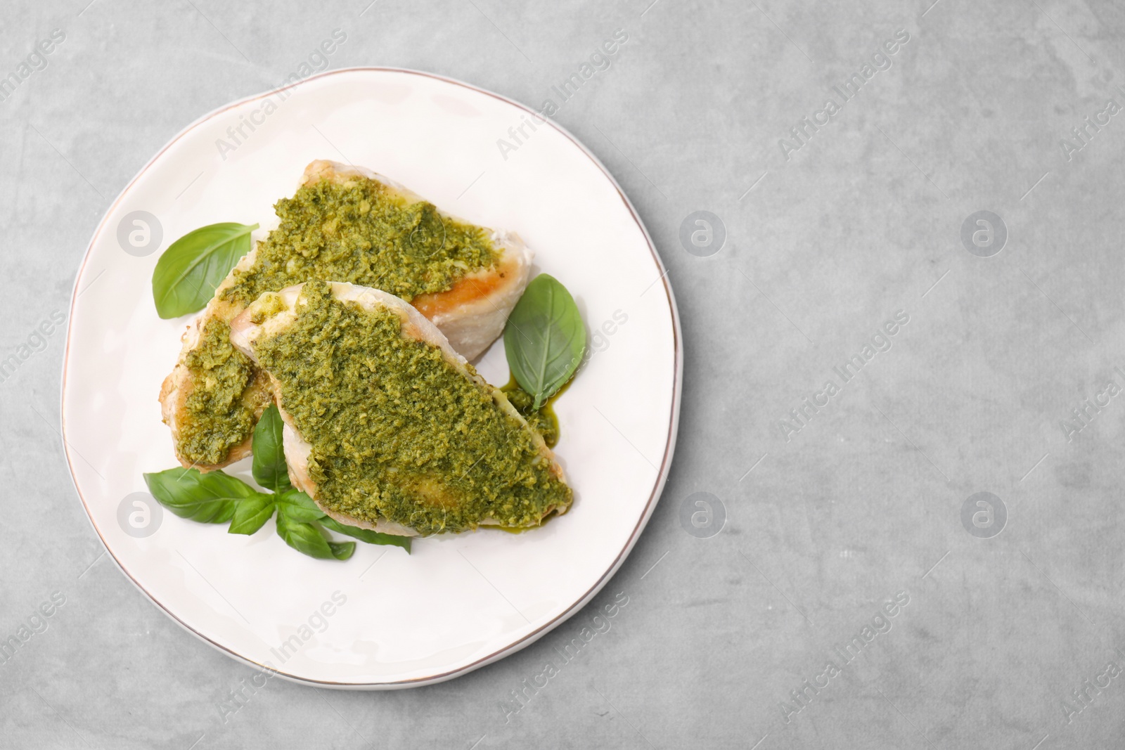 Photo of Delicious chicken breasts with pesto sauce and basil on light gray table, top view. Space for text