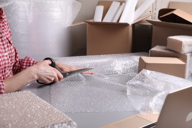 Photo of Woman cutting bubble wrap at table in warehouse, closeup