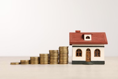 Photo of Mortgage concept. House model and stacks of coins on wooden table against white background, space for text
