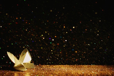 Golden glitter and decorative butterfly against black background. Space for text