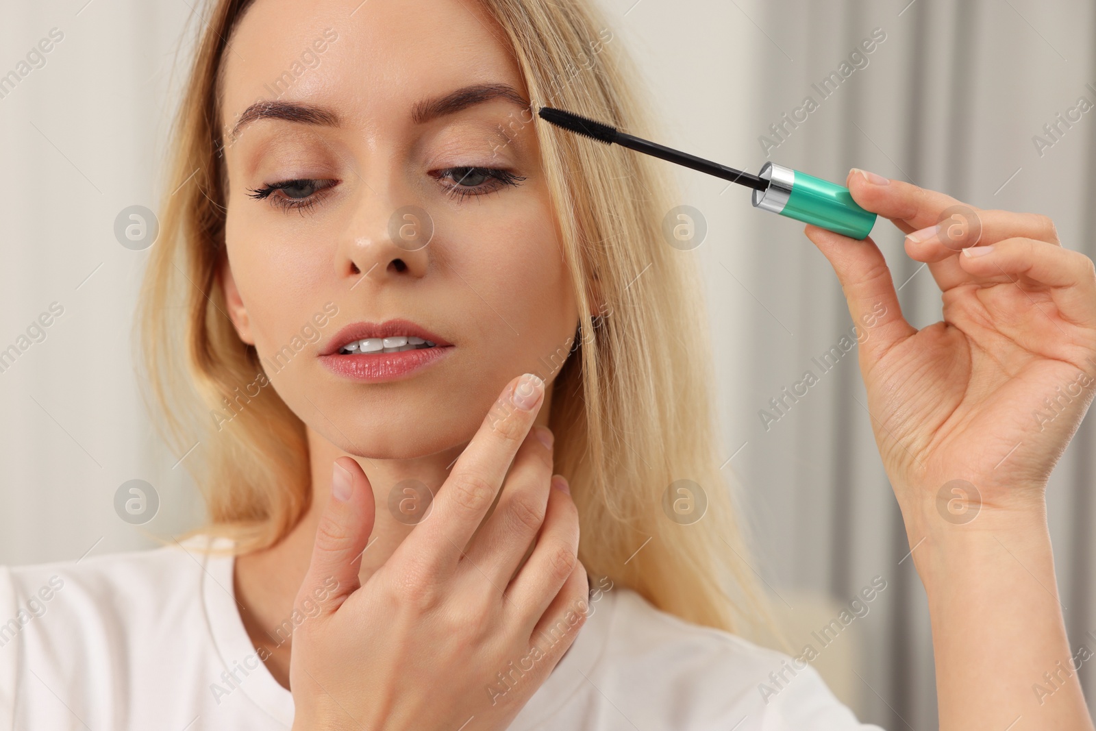 Photo of Beautiful woman applying mascara with brush indoors, closeup