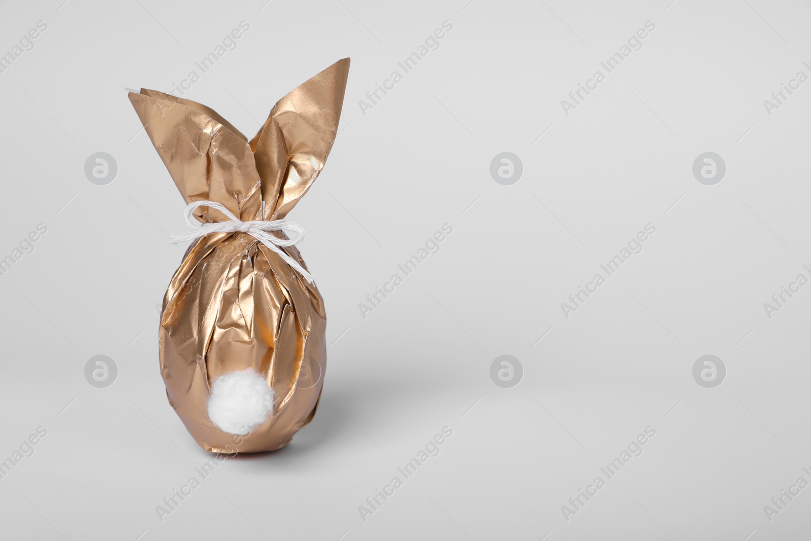 Photo of Easter bunny made of shiny gold paper and egg on white background. Space for text