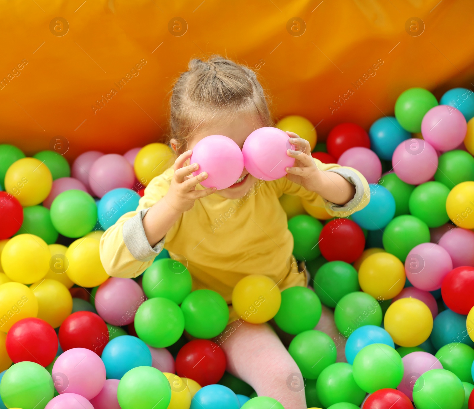 Photo of Cute little child playing in ball pit at indoor amusement park