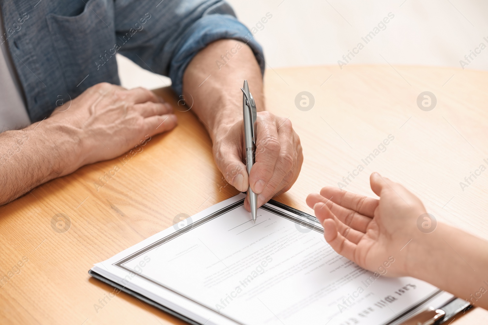 Photo of Notary showing senior man where to sign Last Will and Testament at wooden table indoors, closeup