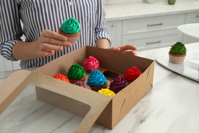 Photo of Woman with box of delicious colorful cupcakes at white marble table indoors, closeup