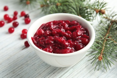 Photo of Bowl of cranberry sauce with fir branches on table, closeup