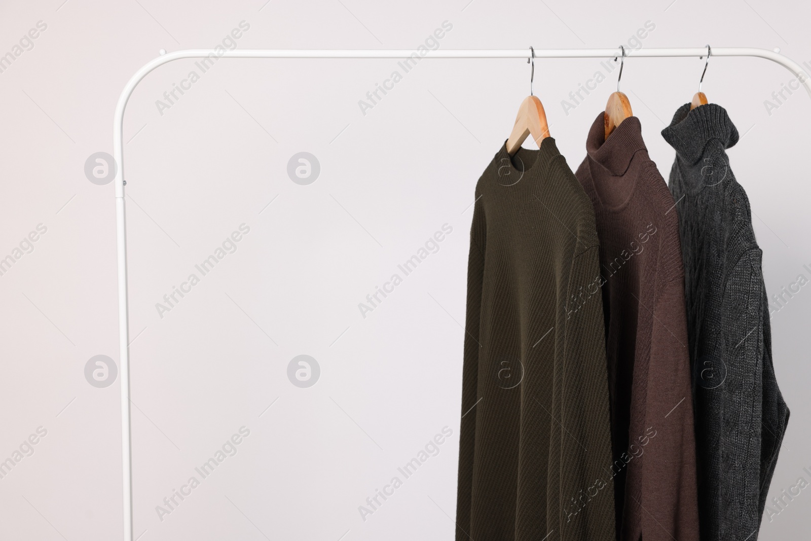Photo of Rack with different casual sweaters on light background. Space for text
