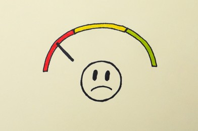 Photo of Sad face and colorful range with pointer drawn on beige background, top view. Emotional management