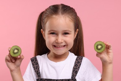 Happy girl with halves of fresh kiwi on pink background