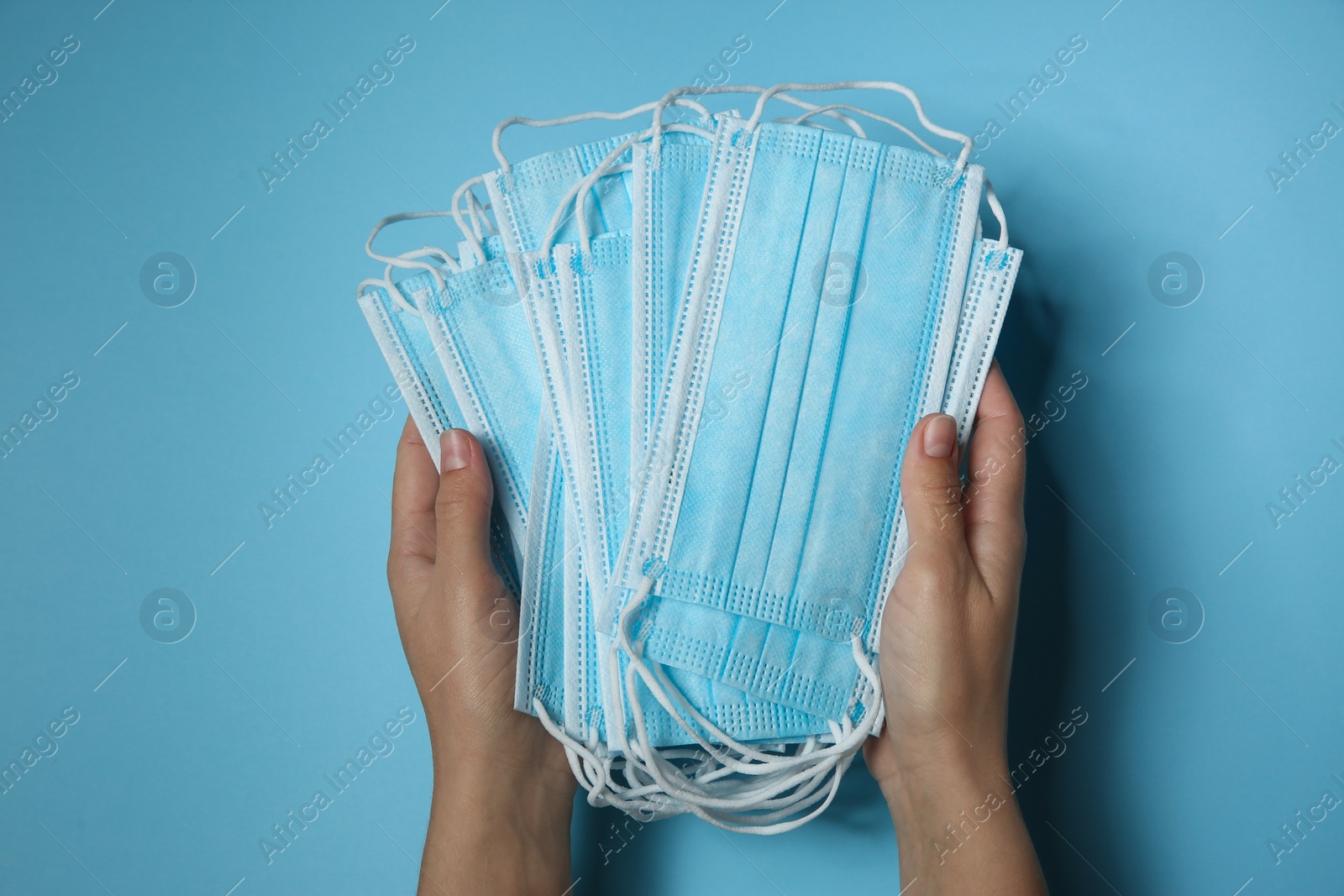 Photo of Woman holding disposable face masks on light blue background, closeup. Protective measures during coronavirus quarantine