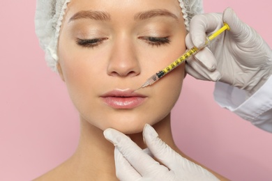 Young woman getting lips injection on color background, closeup. Cosmetic surgery