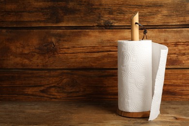 Photo of Holder with roll of white paper towels on wooden table. Space for text