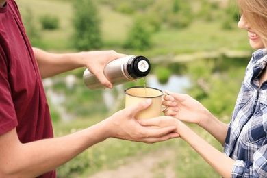 Photo of Man pouring drink into mug for woman outdoors. Camping season