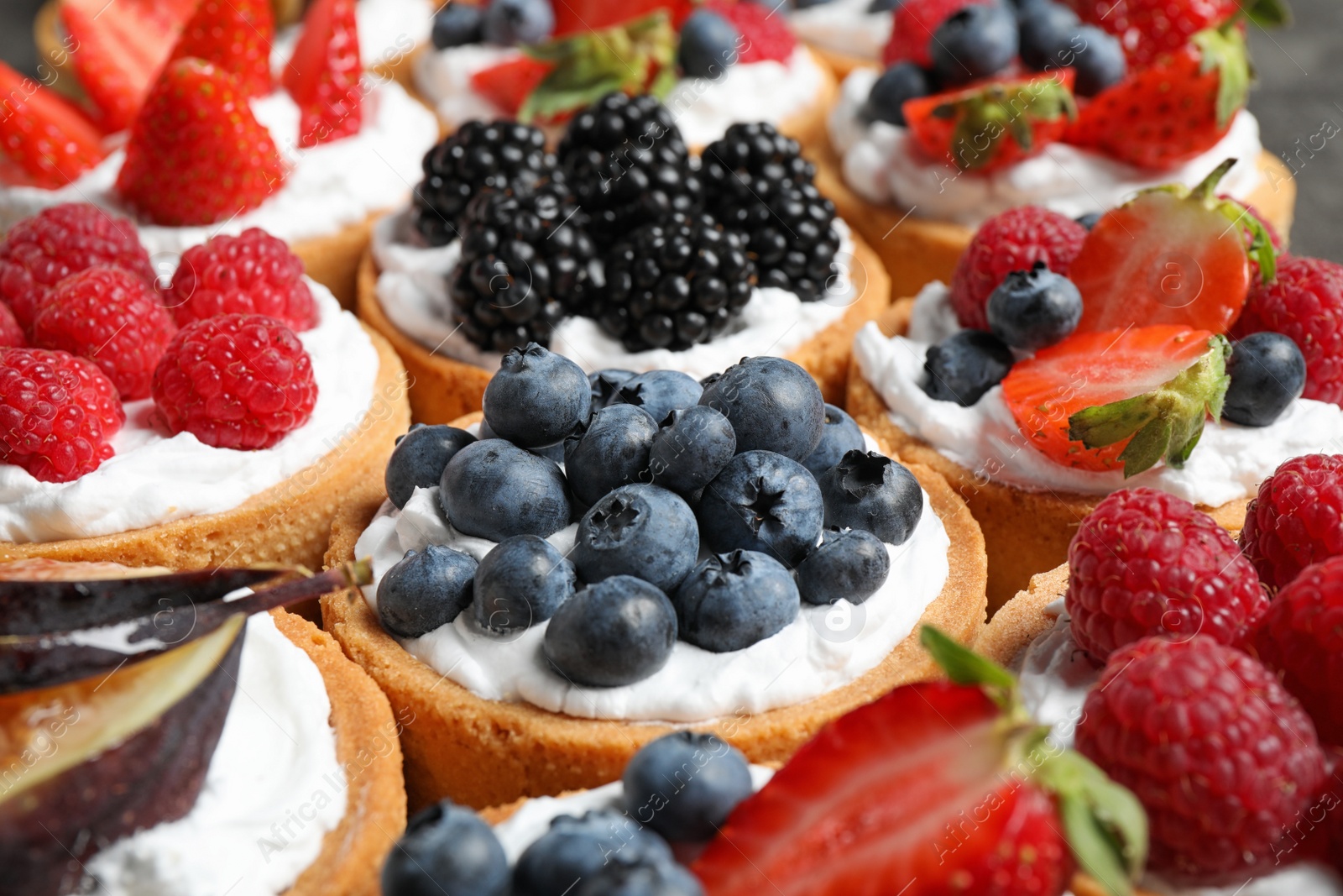 Photo of Many different berry tarts on table, closeup. Delicious pastries