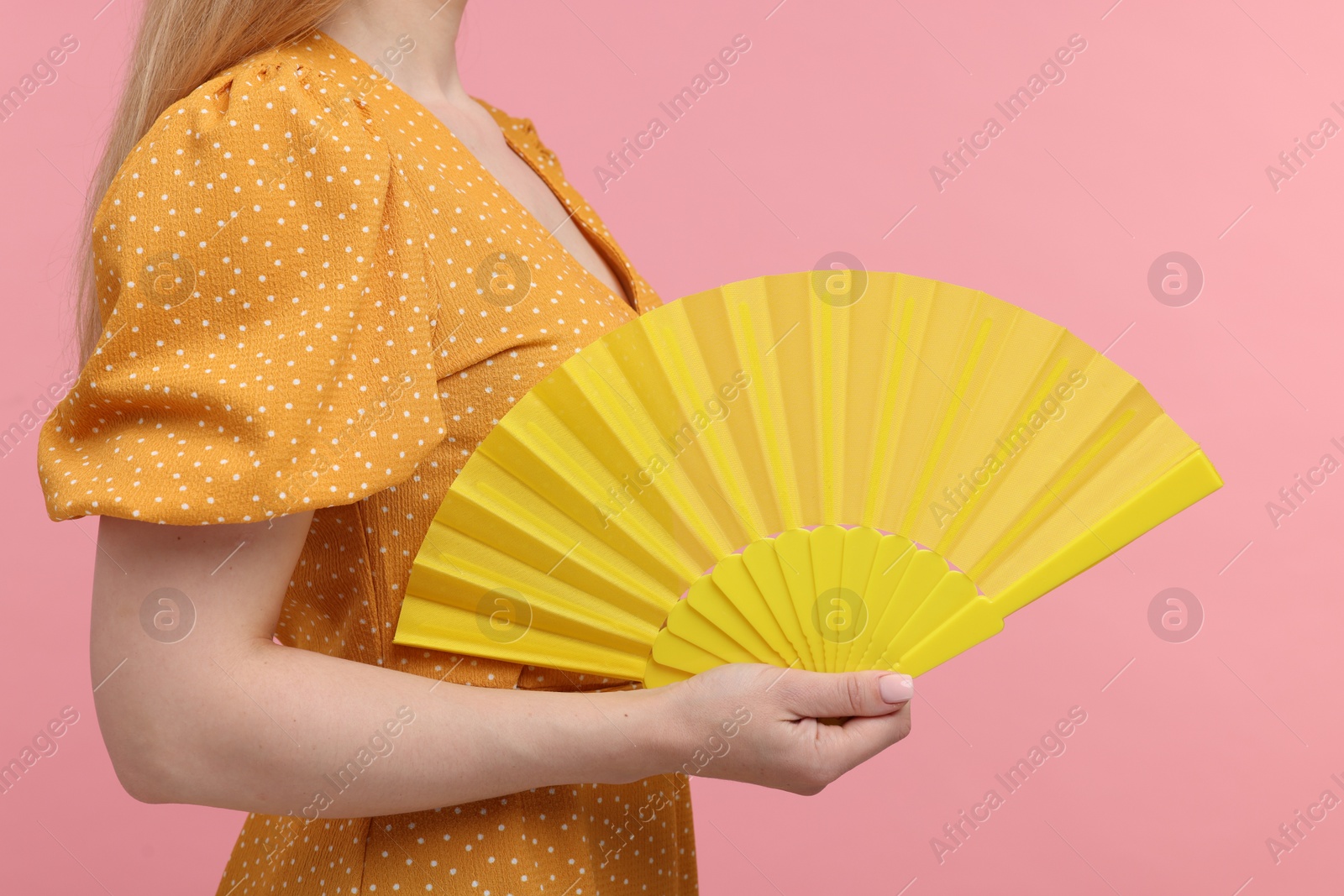 Photo of Woman with yellow hand fan on pink background, closeup