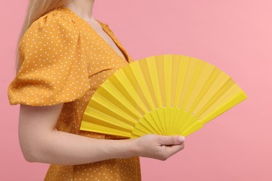 Woman with yellow hand fan on pink background, closeup