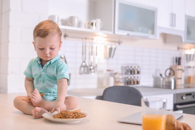 Cute little boy with cookies sitting on table in kitchen