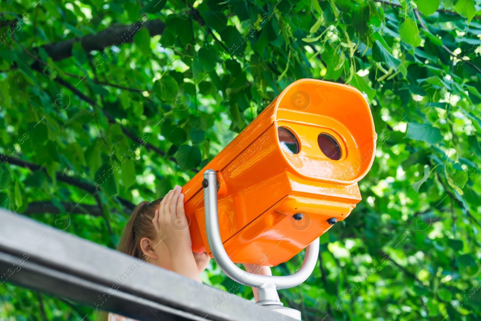 Photo of Girl looking through mounted binoculars outdoors on sunny day