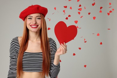 Photo of Young woman with paper heart under confetti on light grey background, space for text