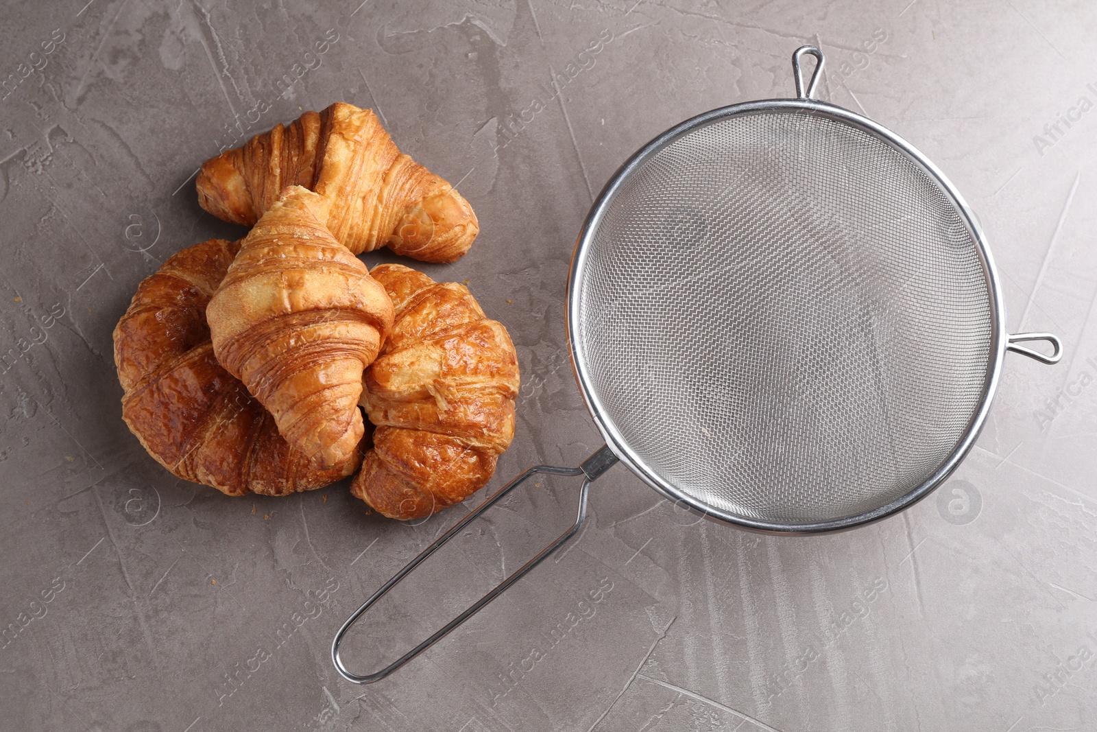 Photo of Clean sieve and croissants on grey textured table, flat lay
