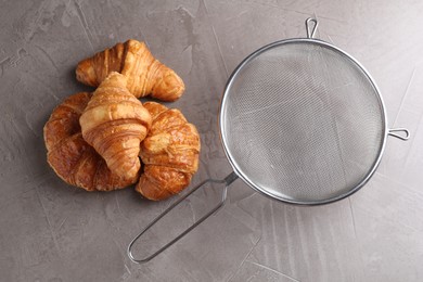 Photo of Clean sieve and croissants on grey textured table, flat lay