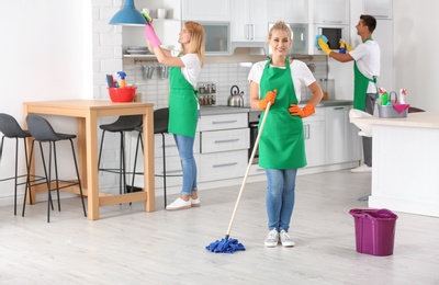 Photo of Team of professional janitors in uniform cleaning kitchen