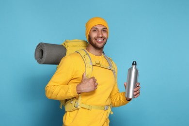 Photo of Happy tourist with backpack and thermo bottle on light blue background