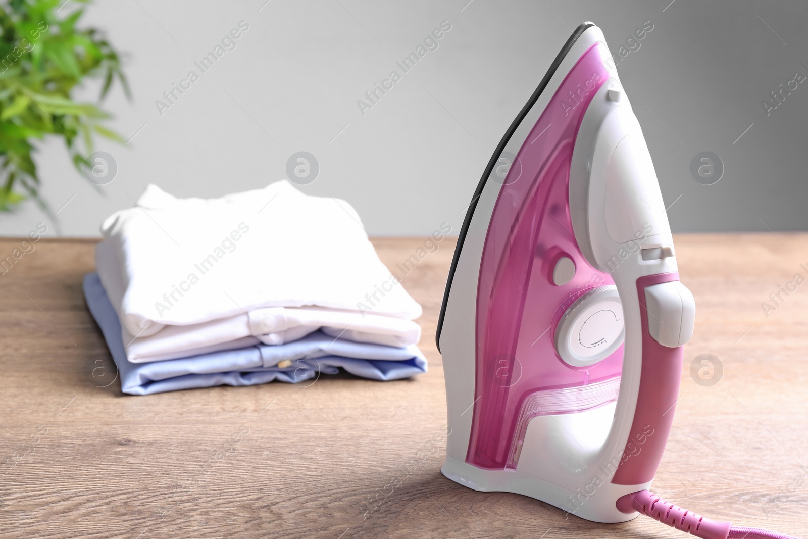 Photo of Modern electric iron and folded clothes on wooden table against light background. Space for text