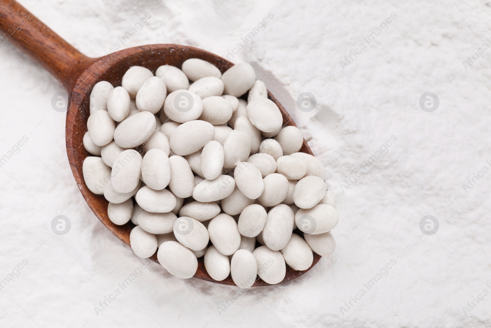 Photo of Wooden spoon with white kidney beans on flour, top view. Space for text