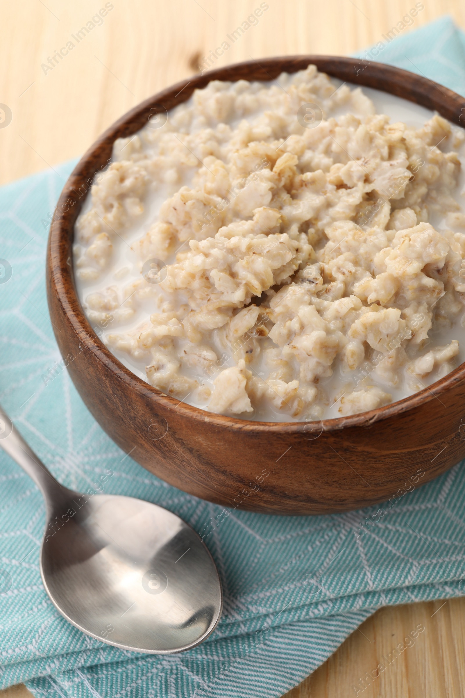 Photo of Tasty boiled oatmeal in bowl and spoon on wooden table, closeup