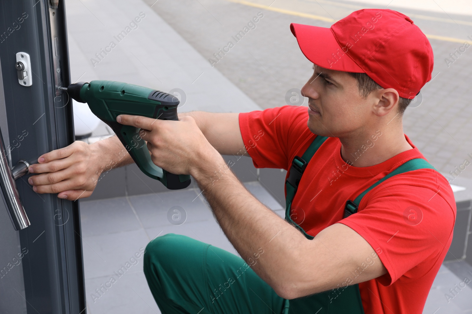 Photo of Handyman with screw gun repairing door lock outdoors