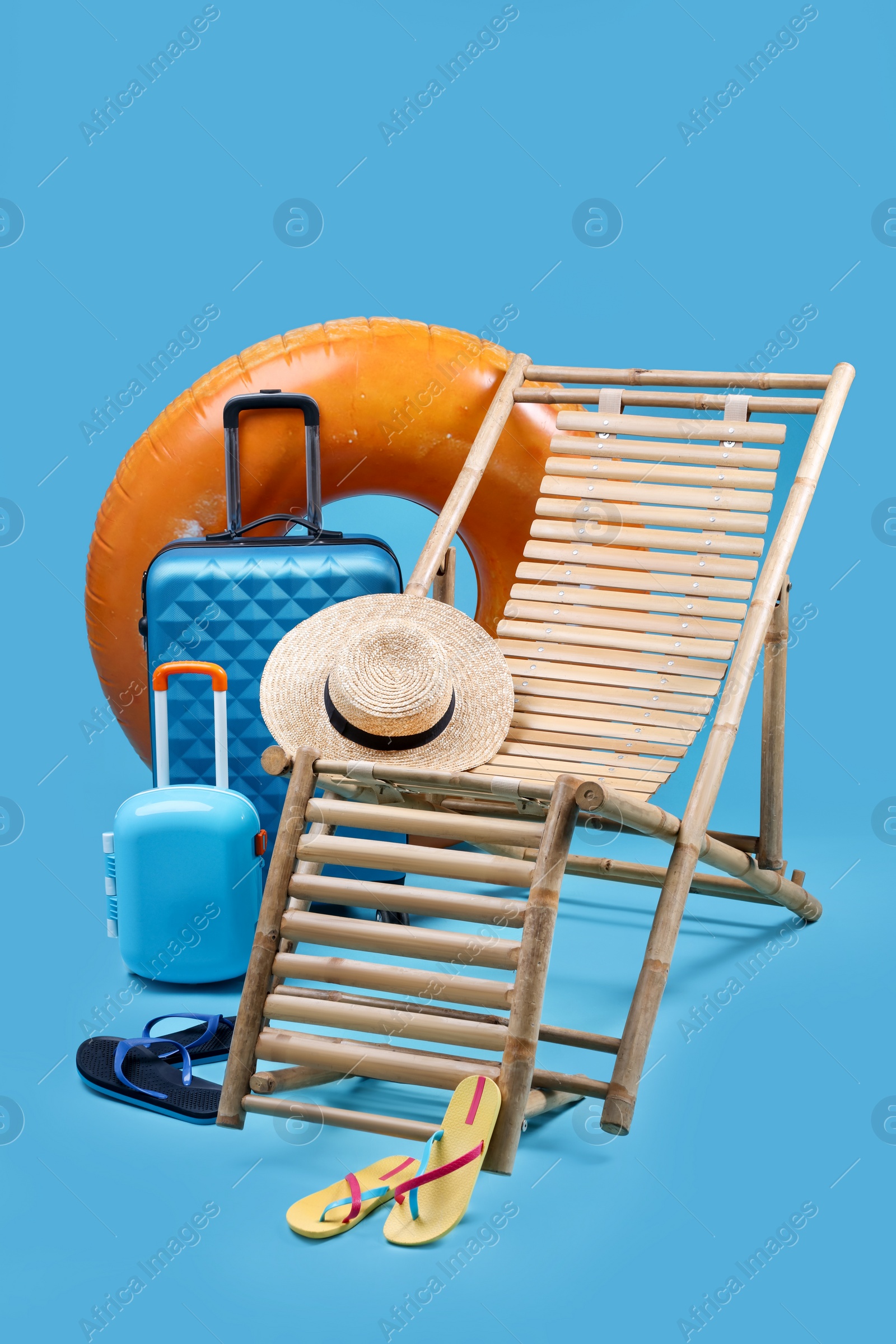 Photo of Deck chair, suitcases and beach accessories on light blue background. Summer vacation