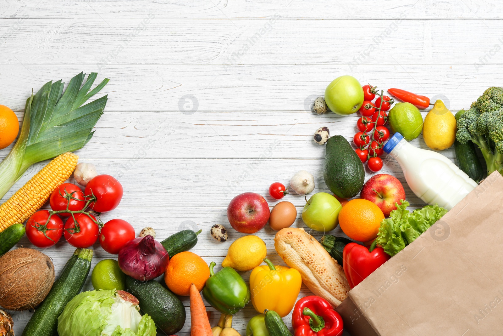 Photo of Paper bag with different groceries on white wooden table, flat lay. Space for text