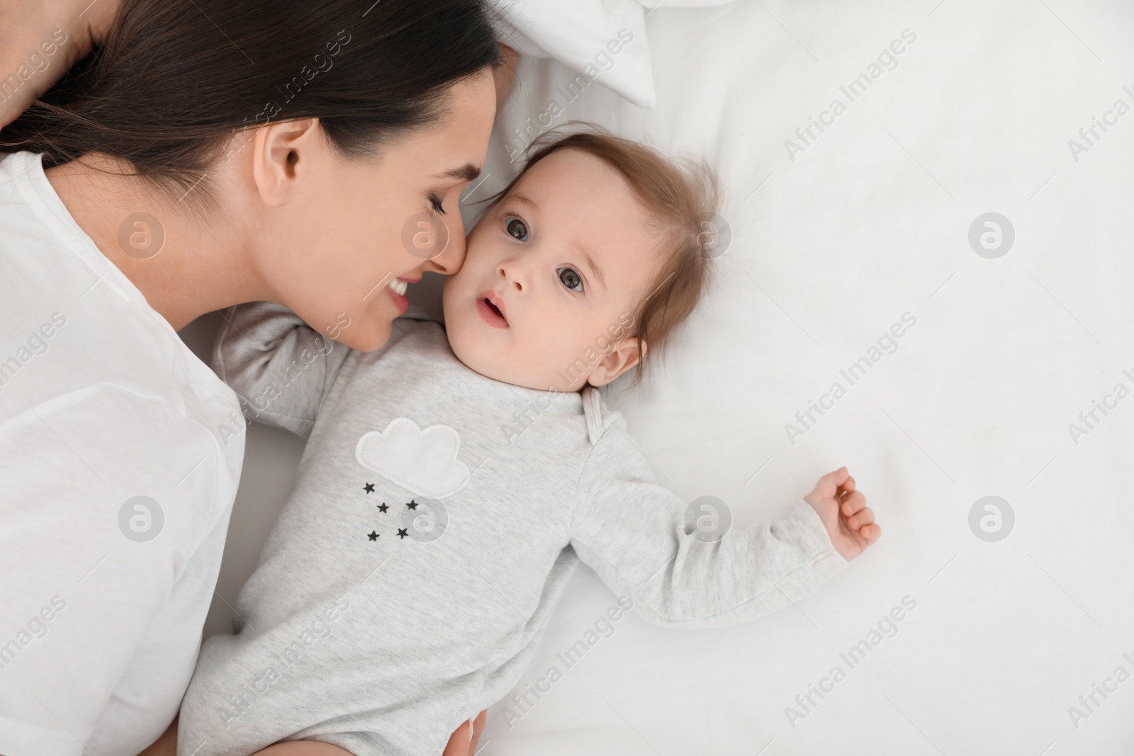 Photo of Cute baby with mother lying on bed, above view. Space for text