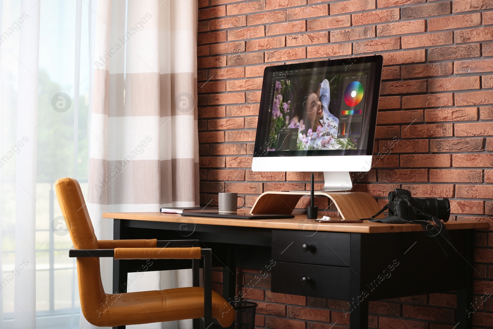 Photo of Modern retoucher's workplace with different digital devices on wooden table near red brick wall