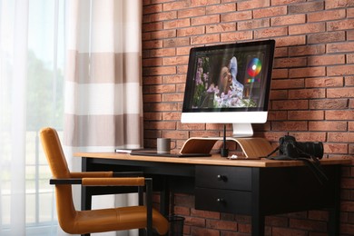 Modern retoucher's workplace with different digital devices on wooden table near red brick wall