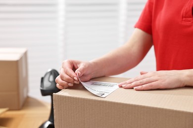 Parcel packing. Post office worker sticking barcode on box indoors, closeup