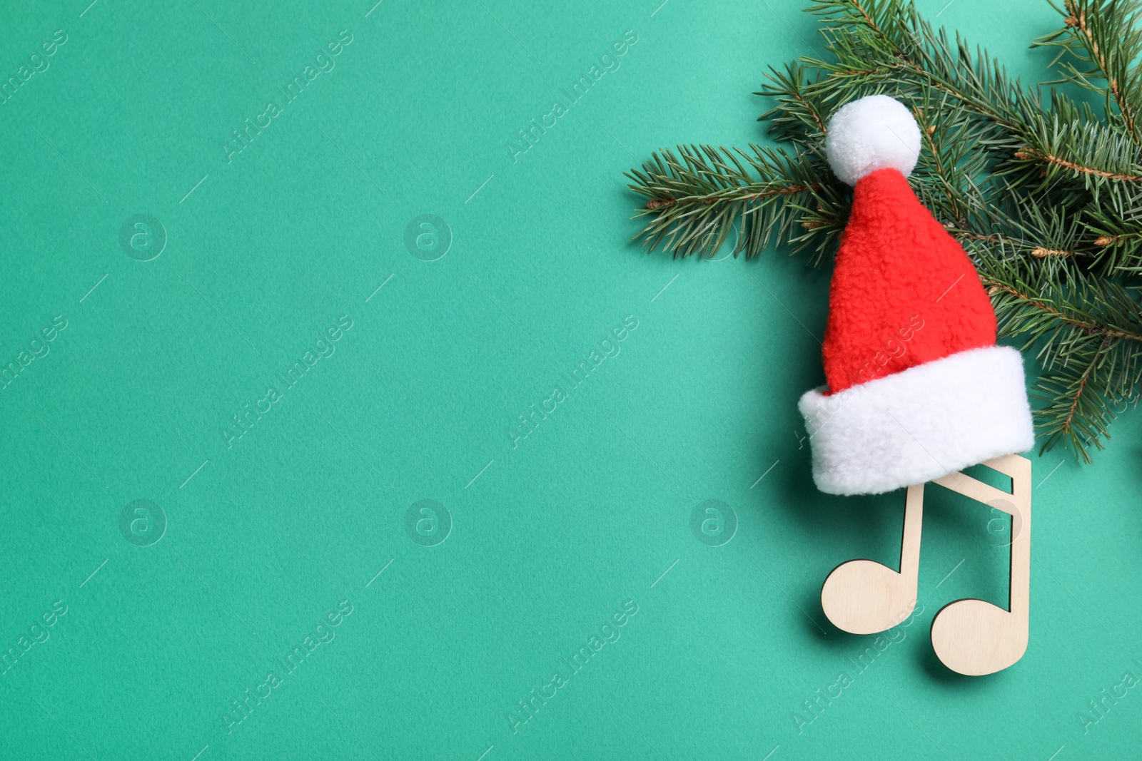 Photo of Wooden music note with Santa hat near fir tree branches and space for text on green background, flat lay. Christmas celebration