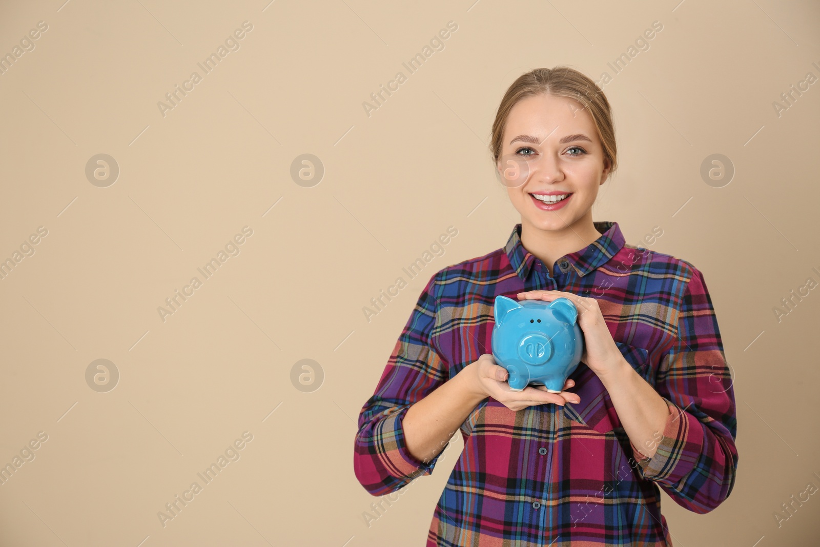 Photo of Happy young woman with piggy bank and space for text on color background. Money saving