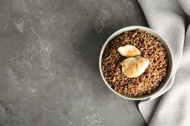 Photo of Tasty buckwheat porridge with meat on grey table, top view. Space for text