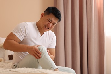 Asian man suffering from knee pain on bed indoors. Space for text