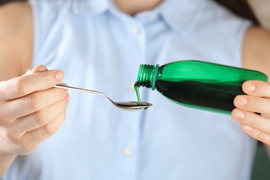 Woman pouring cough syrup into spoon, closeup