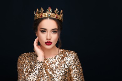 Beautiful young woman wearing luxurious crown on black background, space for text