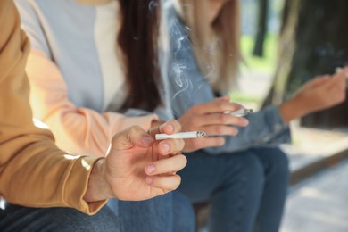 Photo of People with cigarettes outdoors on sunny day, closeup of hands