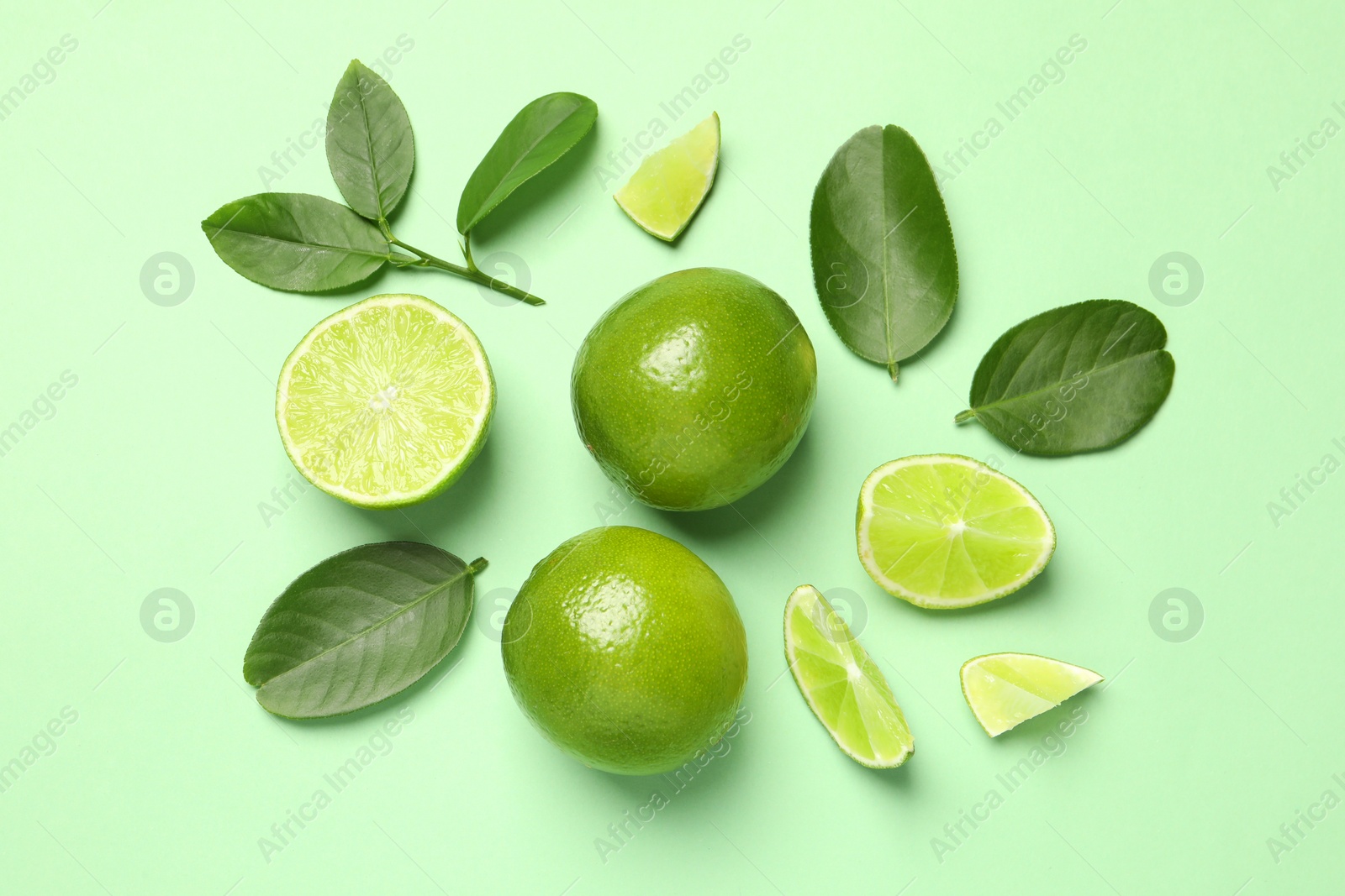 Photo of Whole and cut fresh ripe limes with leaves on light green background, flat lay