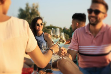Photo of Group of friends having picnic outdoors at sunset, focus on glasses