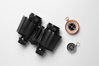 Photo of Modern binoculars and two different compasses on white background, flat lay