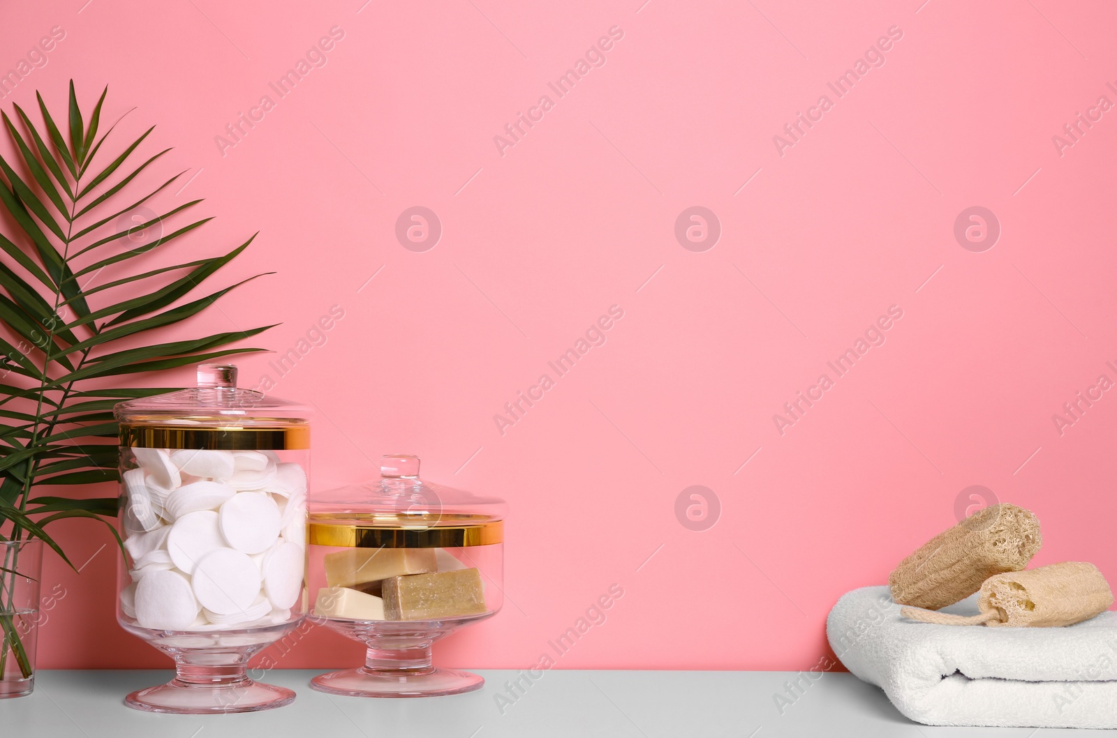 Photo of Composition of glass jar with cotton pads on table near pink wall. Space for text