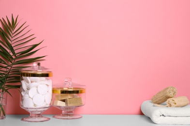 Photo of Composition of glass jar with cotton pads on table near pink wall. Space for text